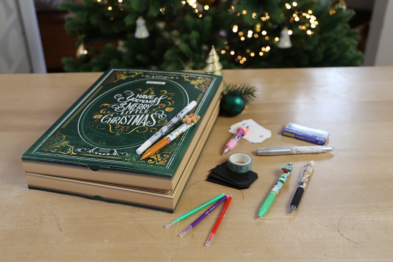 Magic Adventskalender liegt auf Holztisch, daneben liegen Stifte und Washitape